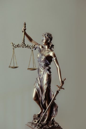 Small bronze statue of lady justice holding the scales, with a beige backgrund