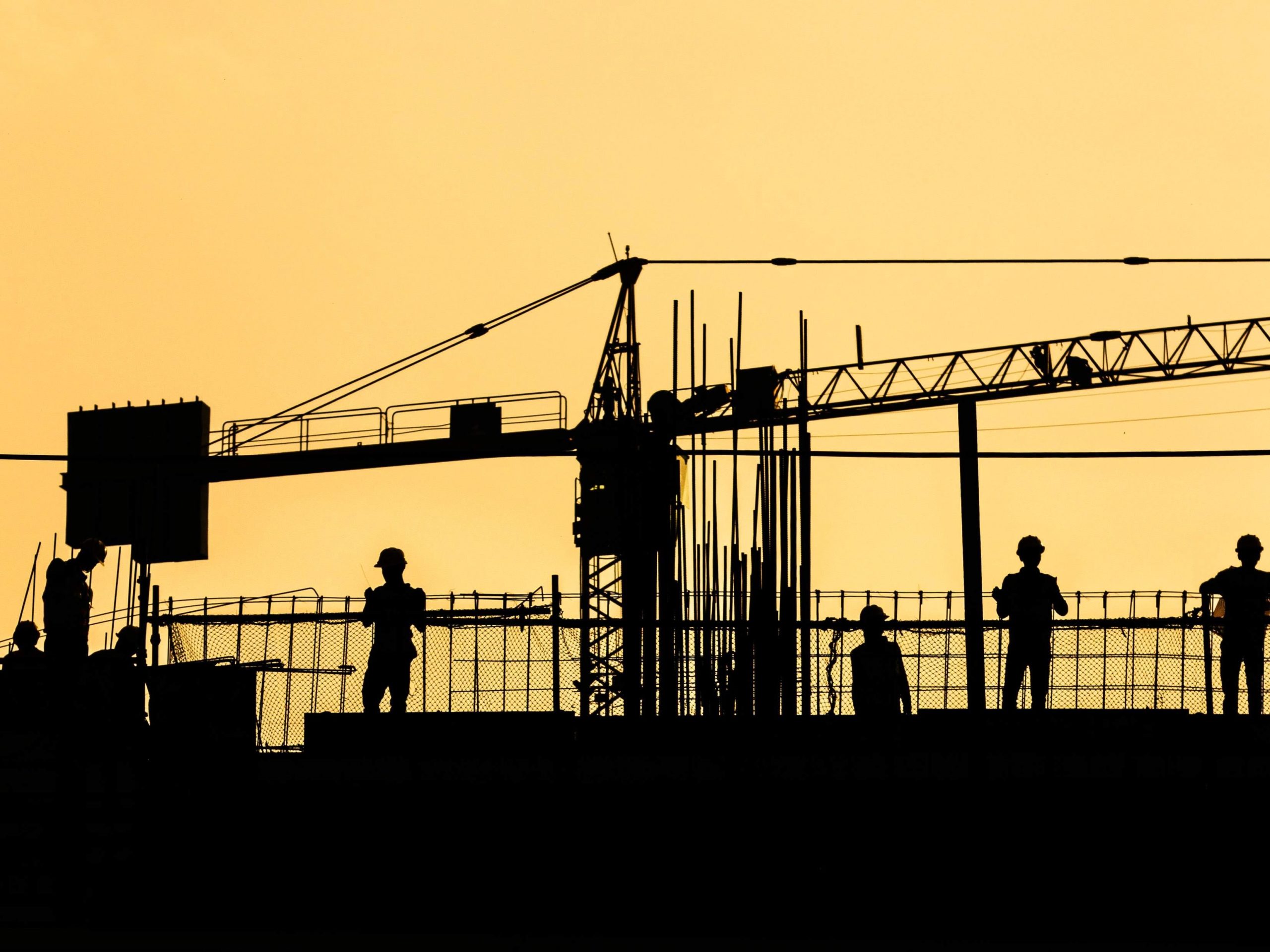 Construction workers on a site, with a crane, situated on the horizon with an overcast of a shadow. 